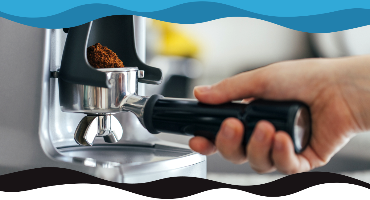 Hand holding a portafilter with coffee at an espresso machine